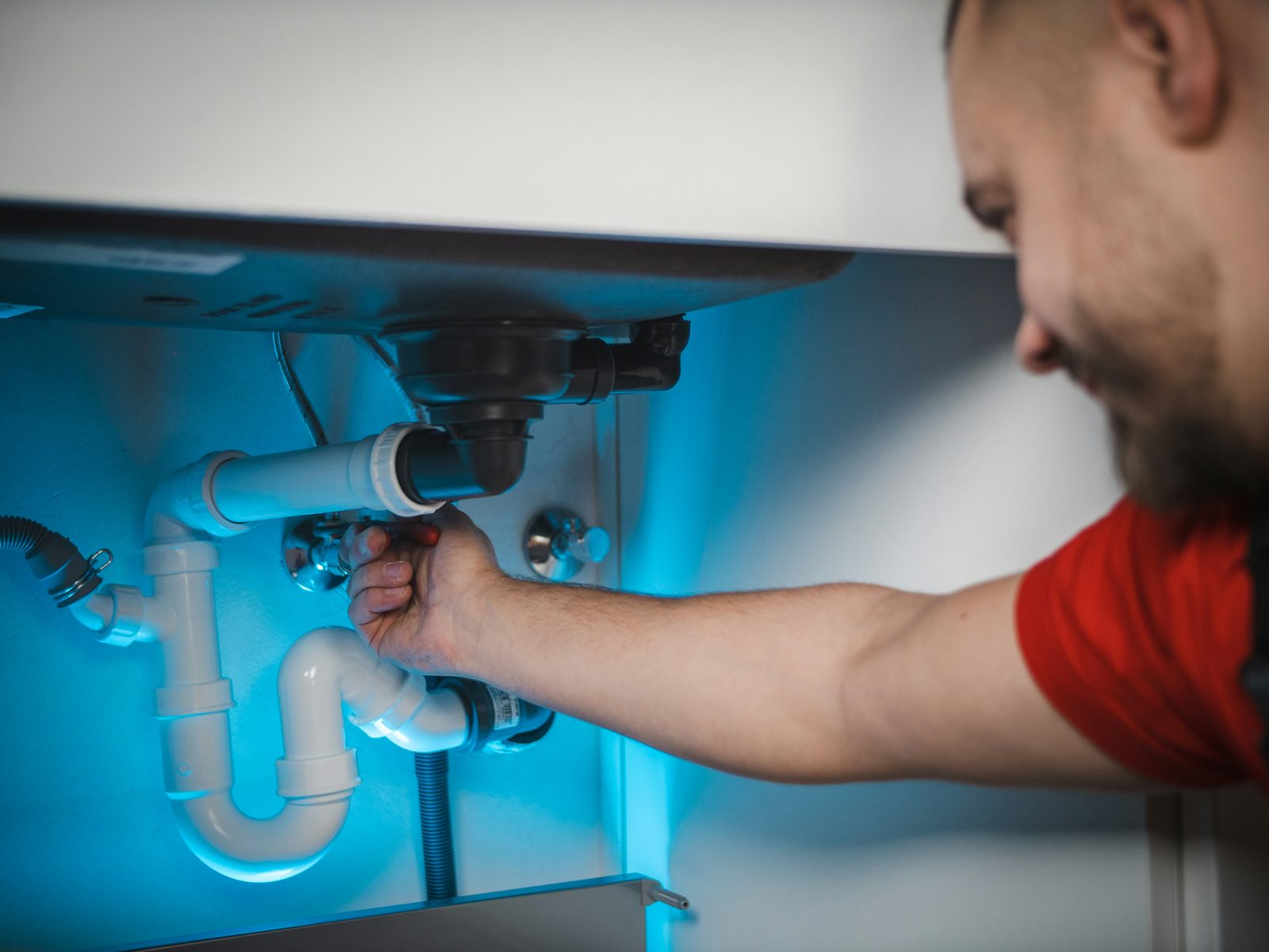 Plumber working on PVC drain pipes under a kitchen sink